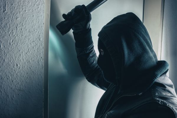 a male intruder is using a flashlight to peer into a window before alarm response services stop him.